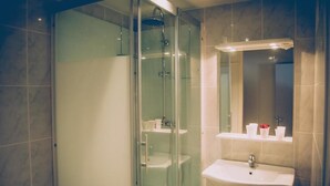 A modern bathroom with a glass-enclosed shower, a white sink, and a mirror above it. - Hotel Restaurant Maurice (Chateauroux)