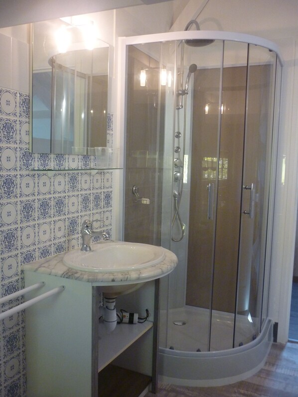 Une salle de bain dotée d’une douche à parois de verre, d’un lavabo blanc avec un plan de toilette en marbre et de carreaux muraux à motifs.