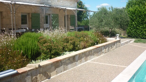 Un bâtiment en pierre avec un toit en tuiles, un espace extérieur abrité avec des sièges et une piscine.
