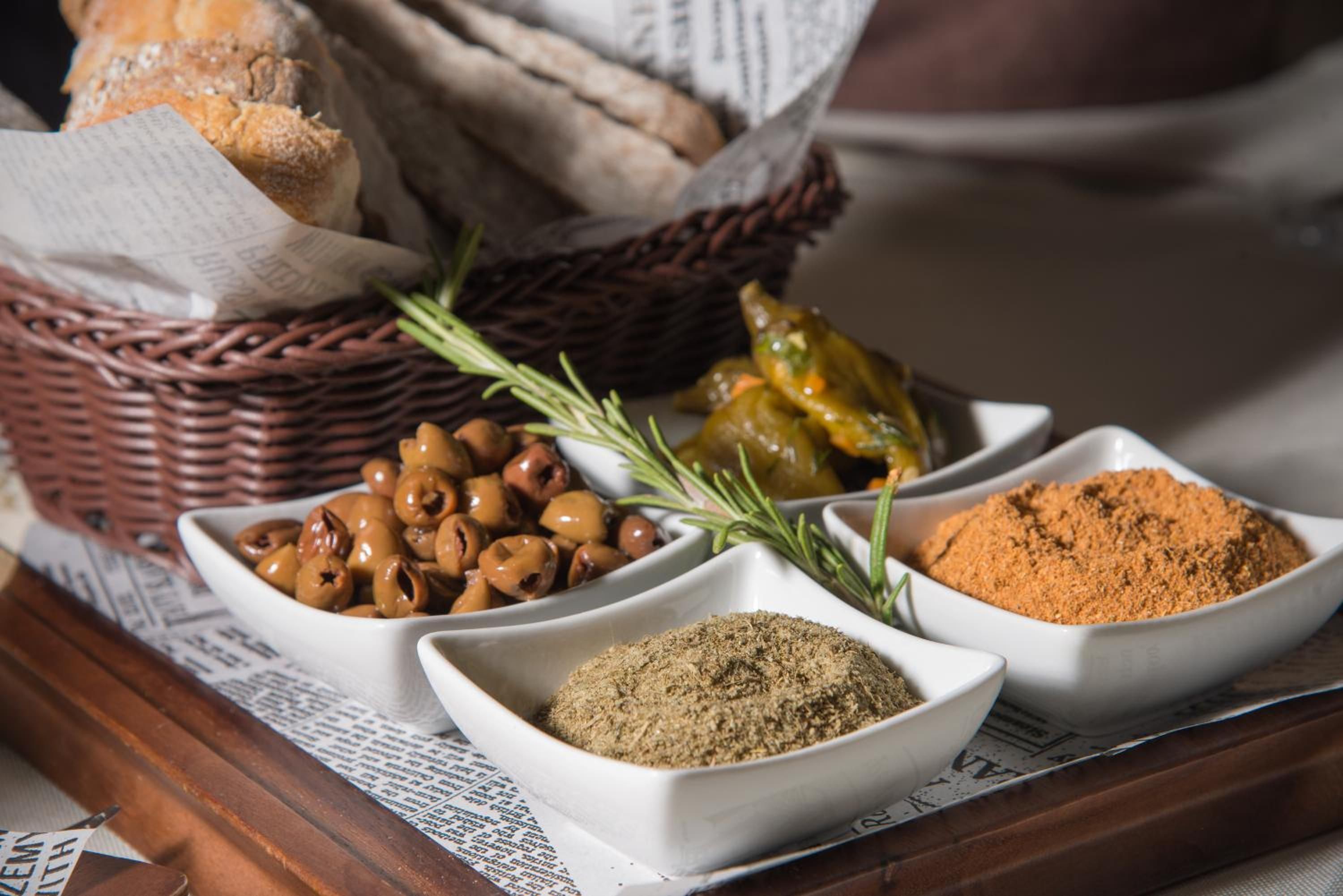 A tray with bread, olives, rosemary, and spices.