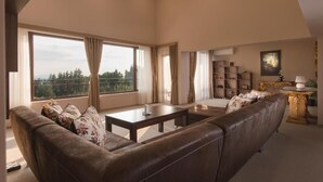 Un salón espacioso con un sofá de cuero, una mesa de centro y una estantería. Amplias ventanas ofrecen vistas al exterior.