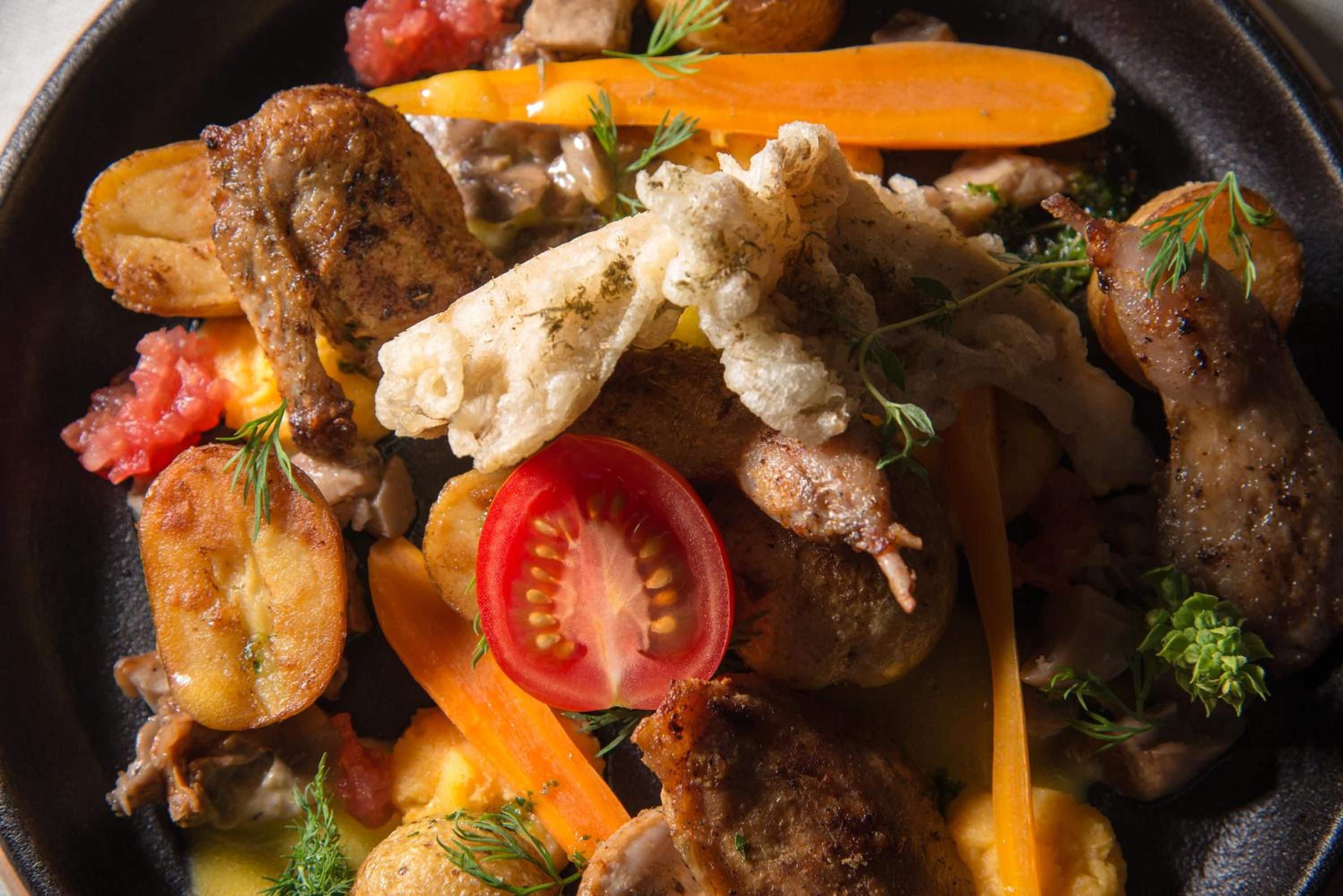 Eine Bratpfanne mit verschiedenen Fleischsorten und Gemüse, darunter Tomaten und Karotten.
