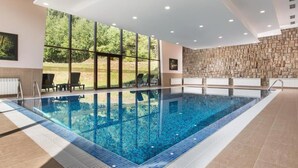 Una piscina interior moderna con paredes de vidrio transparente, piso de baldosas y pared de piedra.