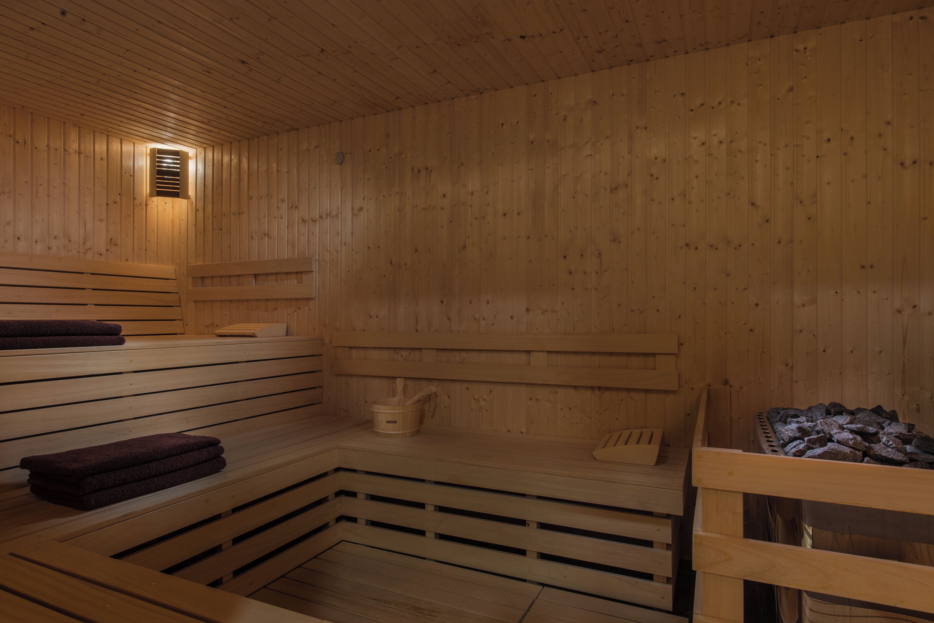 Una sauna con bancos de madera, un calentador para bancos y un recipiente con piedras.