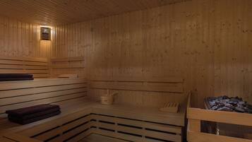 Una sauna con bancos de madera, un calentador para bancos y un recipiente con piedras.