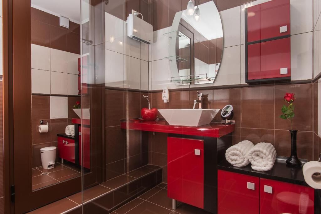 A modern bathroom with a glass shower enclosure, a red vanity with a white sink, and a mirror above the sink.