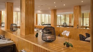 Un interior de madera con una larga barra, sillas tejidas negras y ventanas grandes.