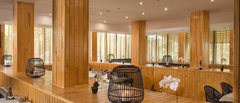 A wooden interior with a long counter, black woven chairs, and large windows.
