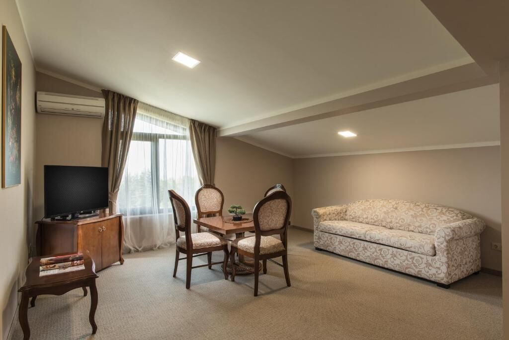 A small, cozy room with a sofa, a TV, a dining table with chairs, and a small cabinet.