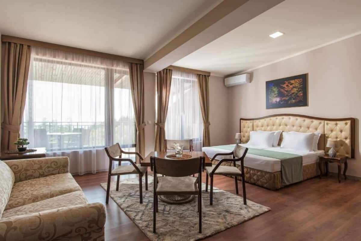 Una habitación de hotel con cama, sofá, mesa de comedor con sillas y ventana con cortinas.