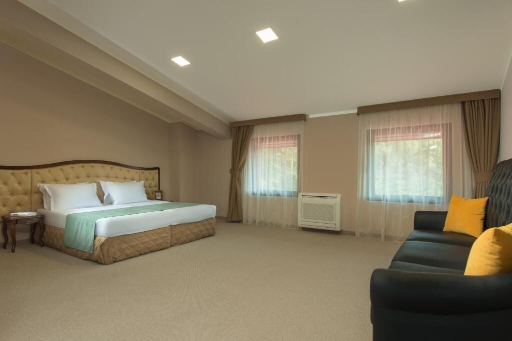 A hotel room with a large bed, a sofa, a nightstand, and a window with curtains.