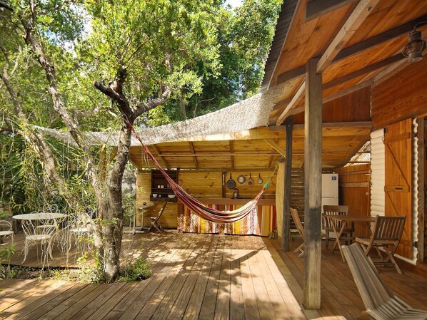Relax in a serene outdoor space with a hammock, tables, and chairs, surrounded by a wooden fence and a charming building in the background.