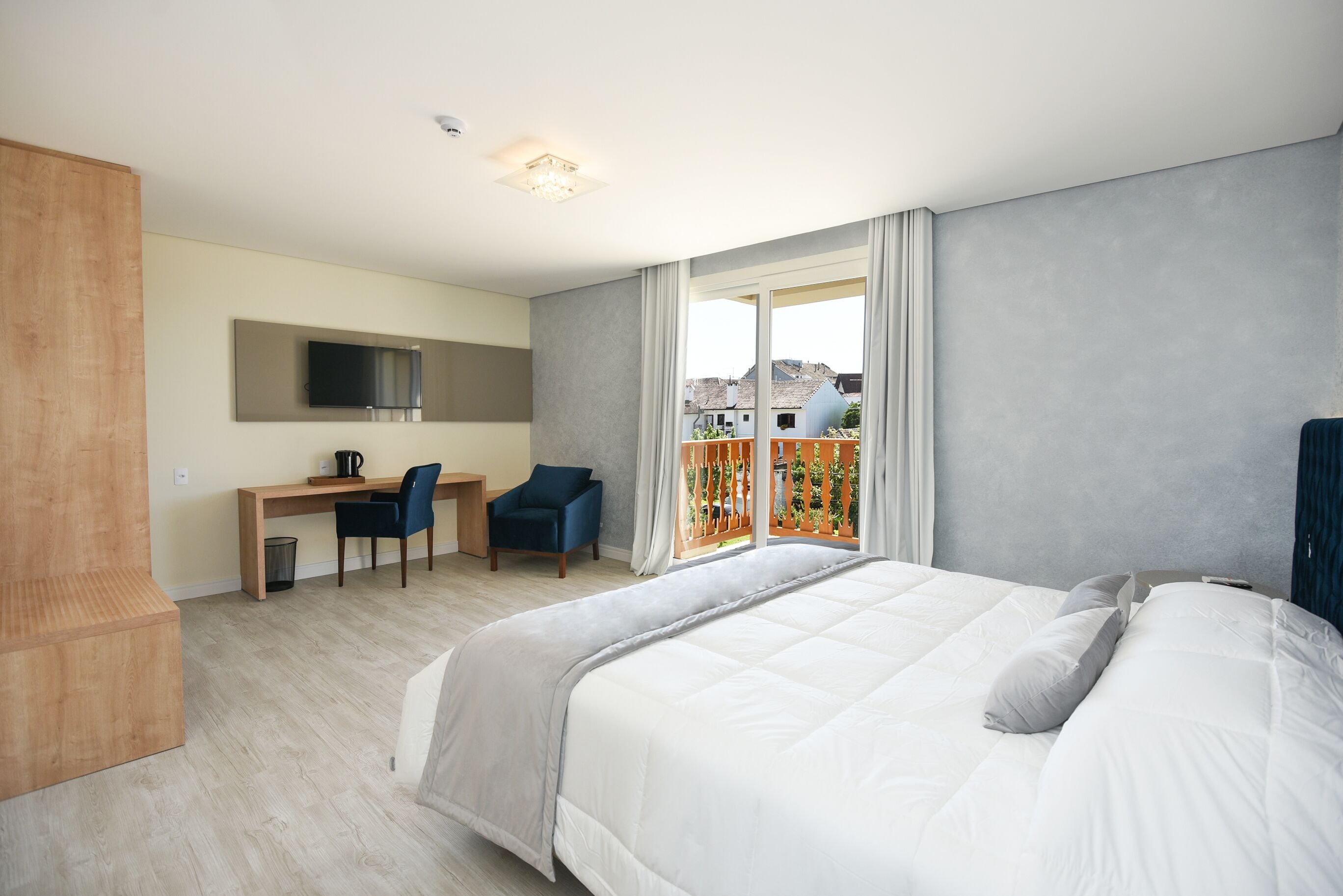 Una habitación de hotel moderna con una cama grande, un escritorio con una silla, televisión y un balcón con vistas a edificios.