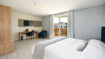 Una habitación de hotel moderna con una cama grande, un escritorio con una silla, televisión y un balcón con vistas a edificios.