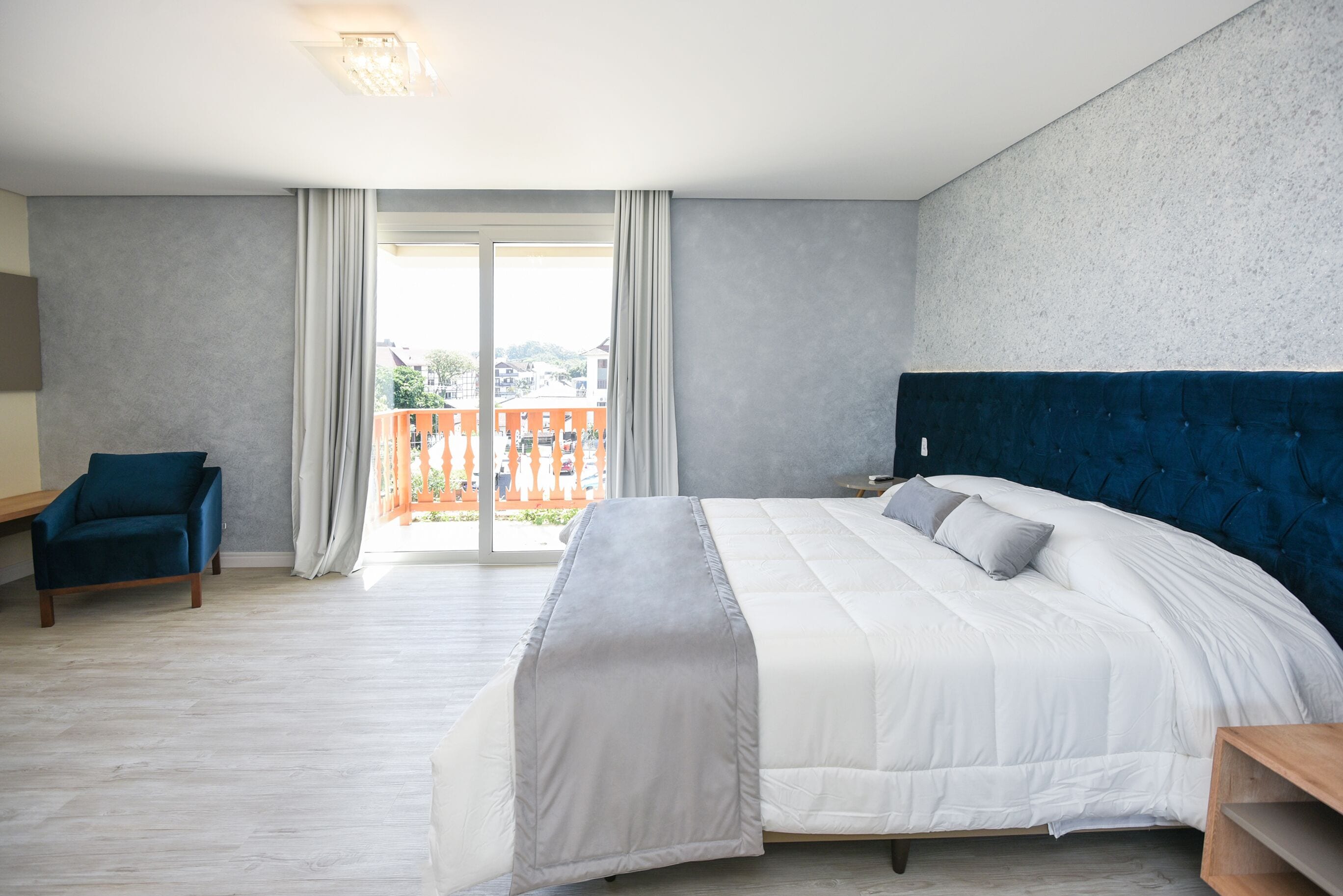 A bedroom with a large bed, a chair, a nightstand, and a view of the outdoors.