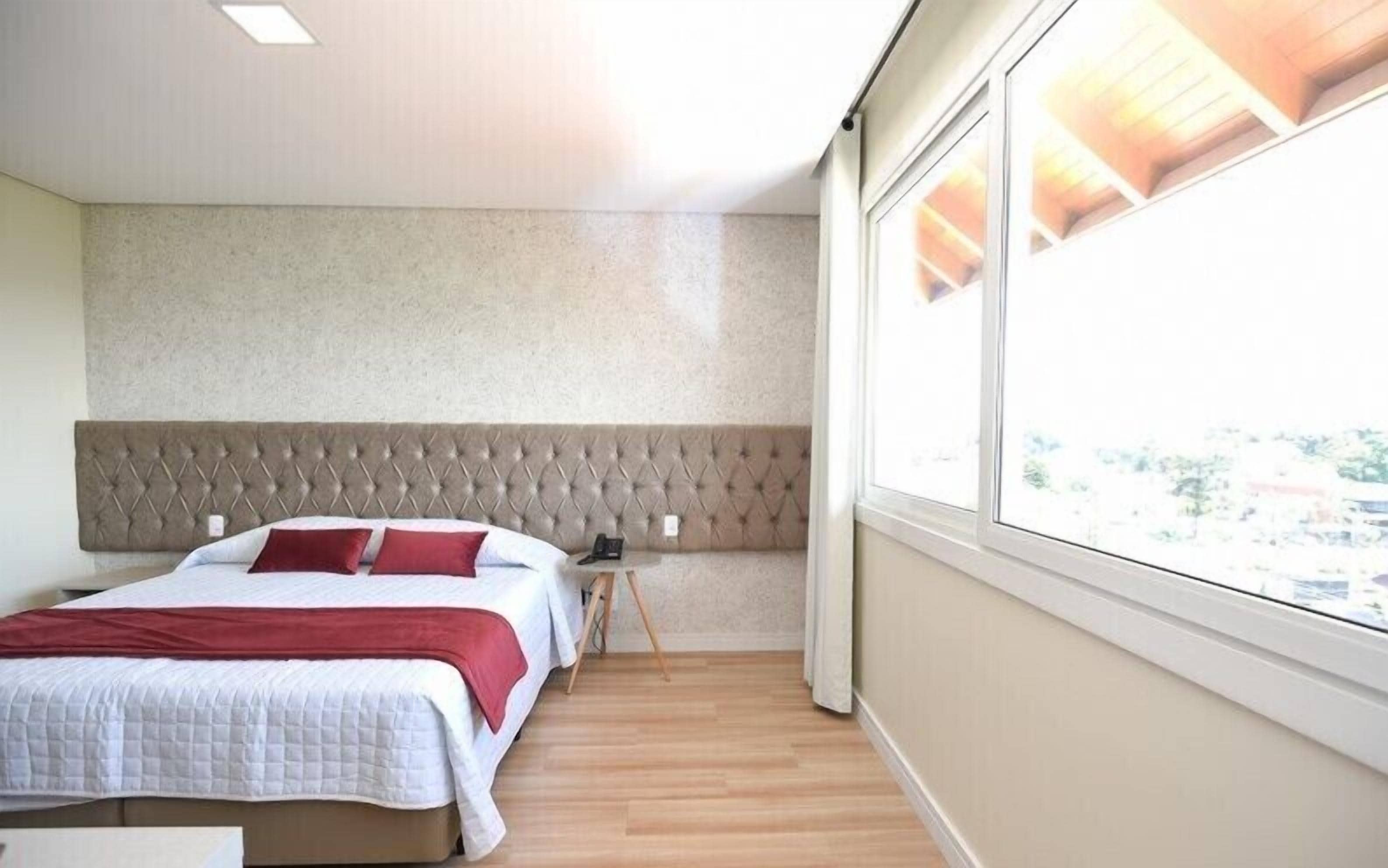A hotel room with a large bed, a headboard, a bedside table, and a window with a view.