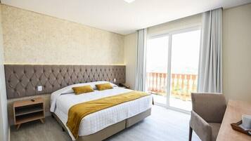 A modern hotel room with a large bed, a wooden nightstand, a desk with a chair, and a balcony with a view.