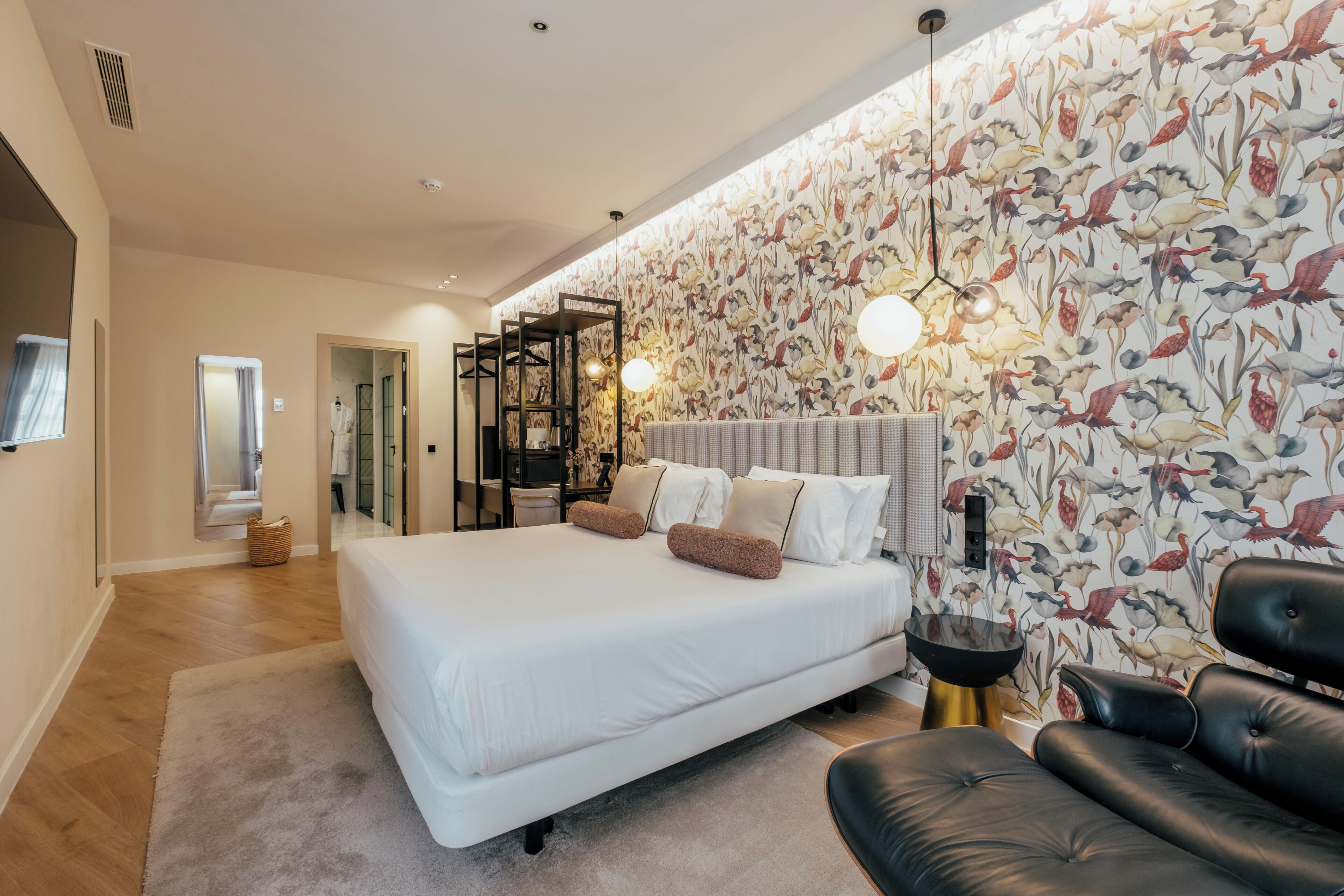 Une chambre moderne avec un grand lit, un canapé en cuir noir et un mur orné d’un motif représentant des oiseaux.