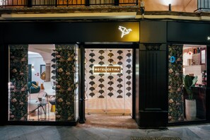 Entrada de hotel con diseño moderno, destacada por un muro con textura y un letrero de neón.