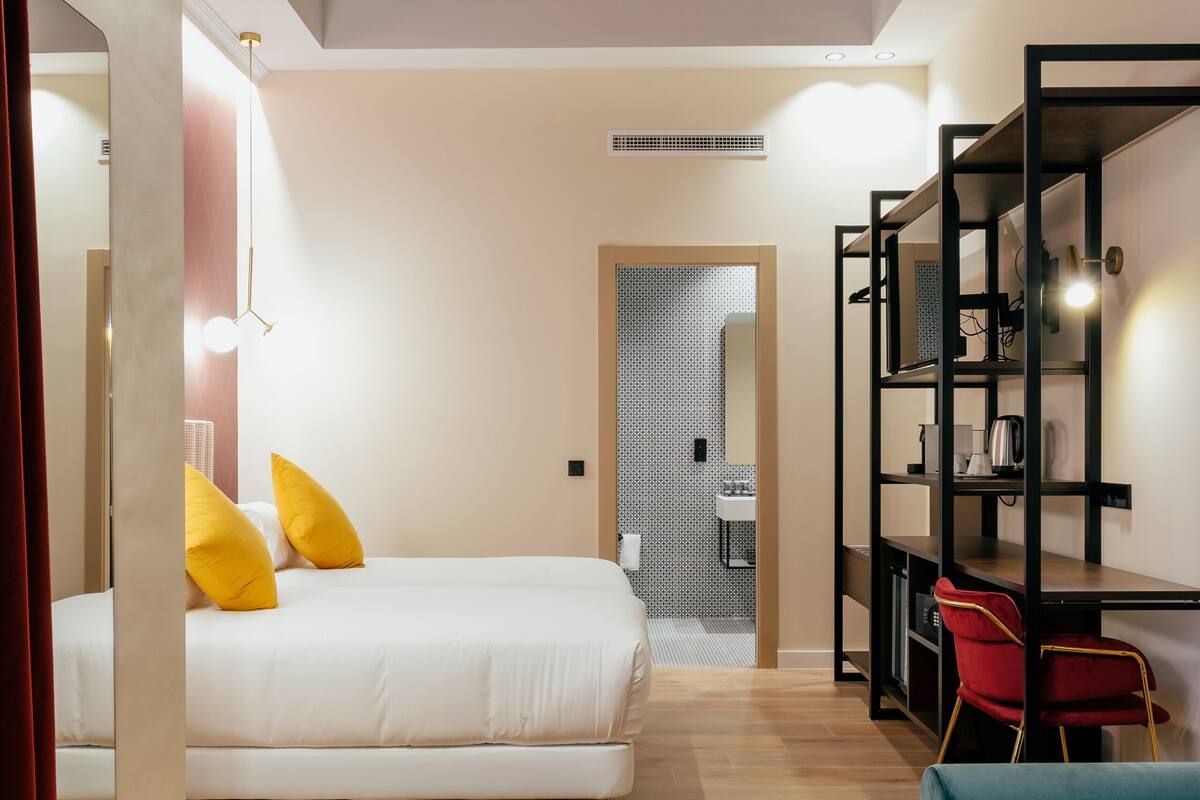 A modern hotel room with a bed, a desk, a chair, and a sofa.