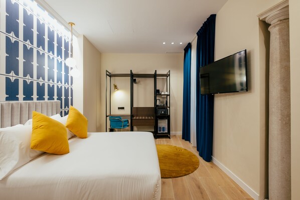 A hotel room with a bed, a desk, a chair, a TV, and a wardrobe.
