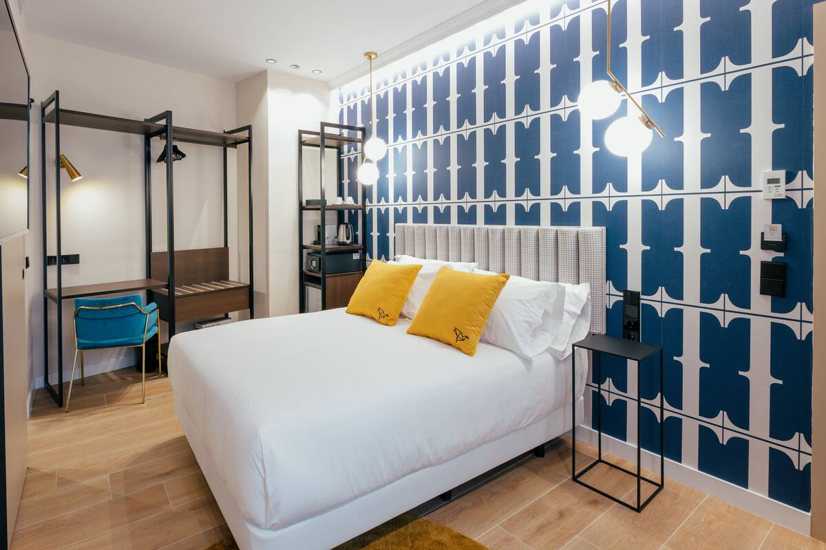 A modern bedroom with a large bed, a wardrobe, a desk, and a blue patterned wall.