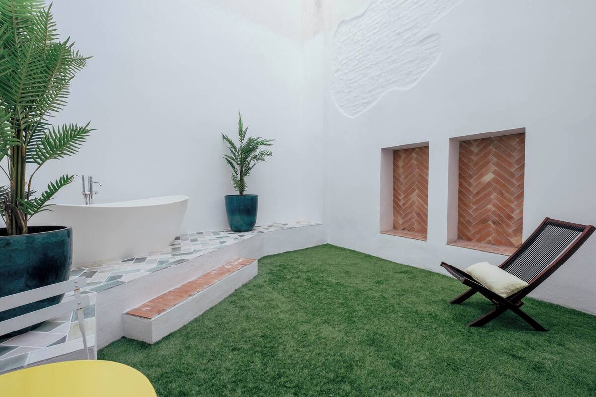 A modern bathroom with a freestanding bathtub, a small step-up area, and a green artificial grass floor.