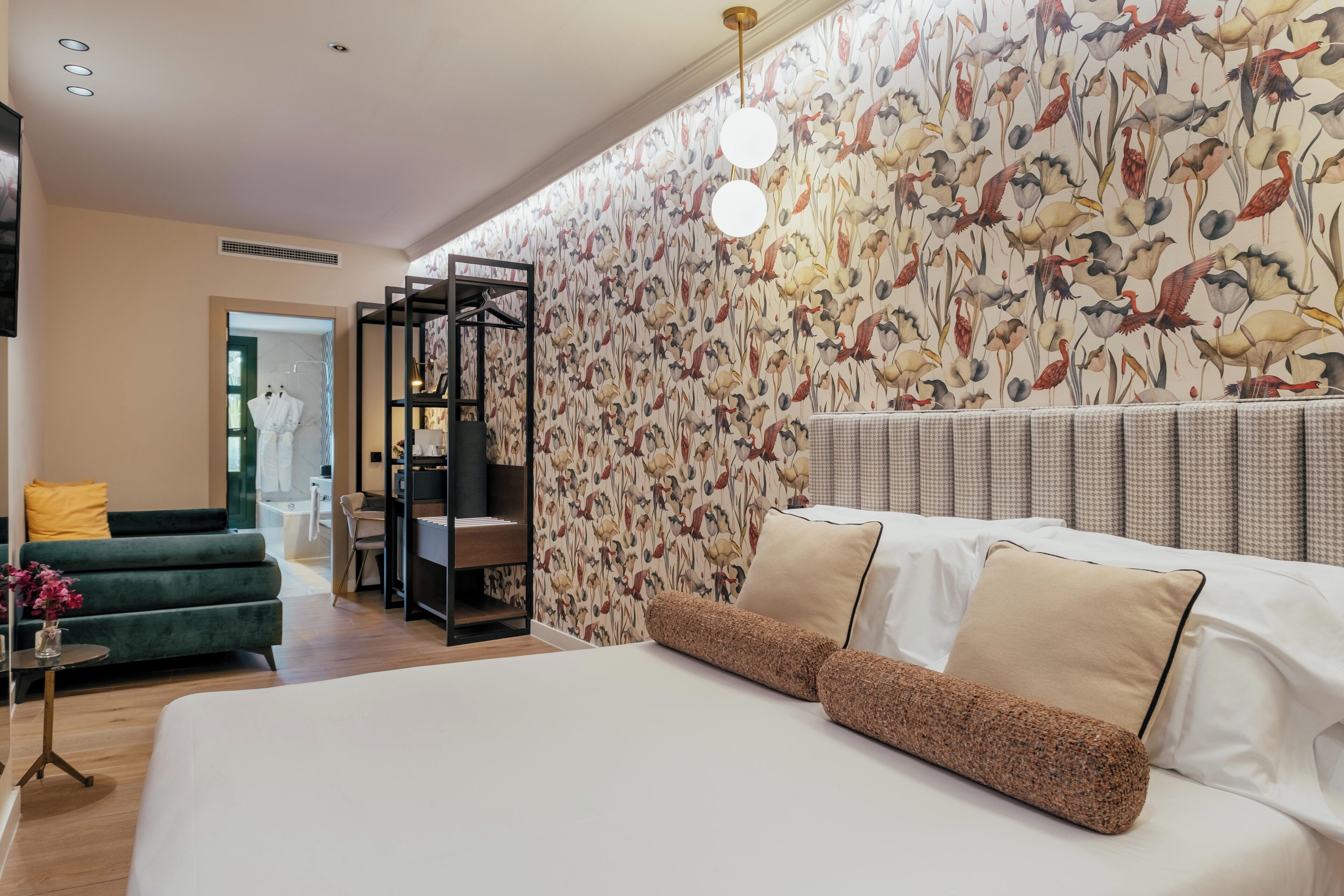 Um quarto moderno com uma cama grande, um sofá verde e uma parede com um padrão de pássaros.