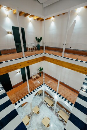 Un interior de varios niveles con un espacio central abierto, rodeado de mesas y sillas, vigas de madera y piso de baldosas.