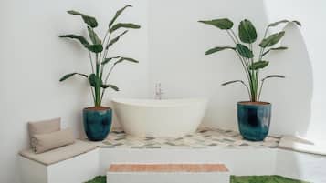 Un baño con una bañera independiente, dos plantas en macetas, un banco y un escalón pequeño que conduce a un suelo de baldosas.