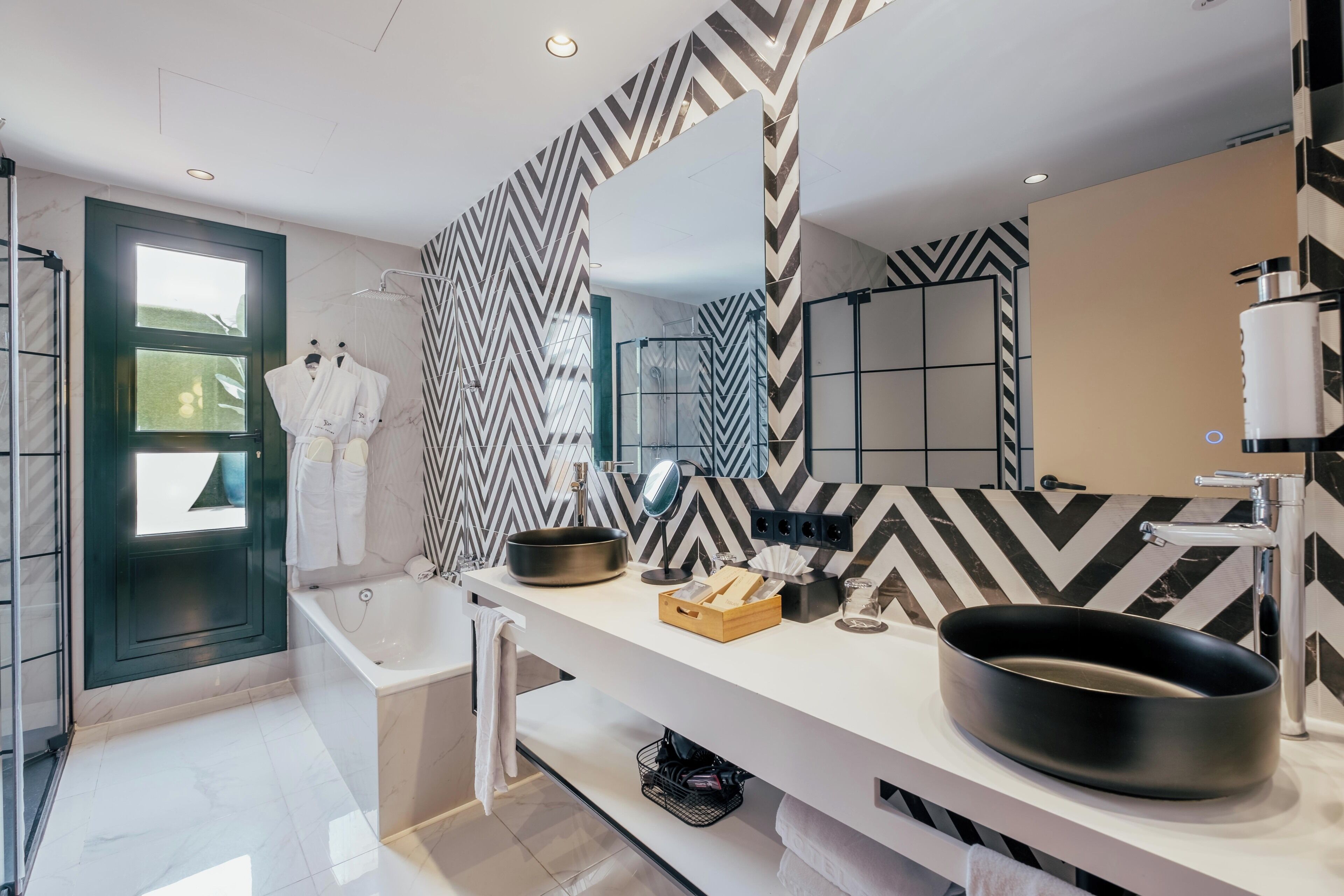 A modern bathroom with a black and white chevron patterned wall, a large mirror, a black sink, and a shower area.