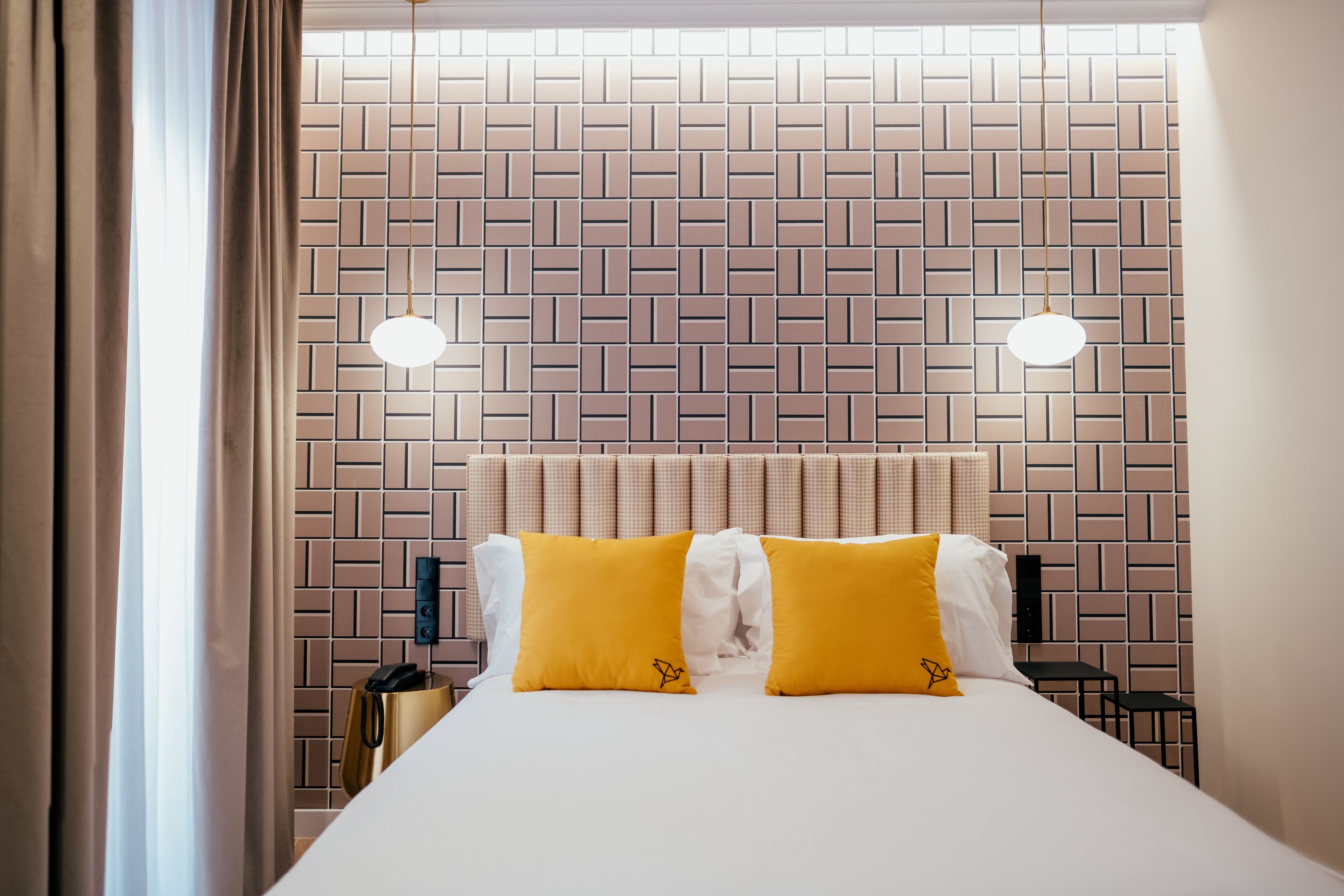 Habitación de hotel con cabecera de ladrillo, dos lámparas de noche y cama con almohadas amarillas y blancas.