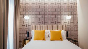 Habitación de hotel con cabecera de ladrillo, dos lámparas de noche y cama con almohadas amarillas y blancas.