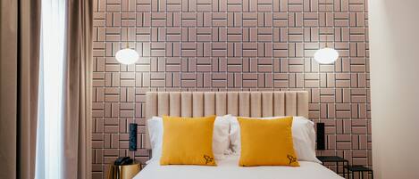 Une chambre d’hôtel avec une tête de lit ornée d’un motif en briques, deux lampes de chevet et un lit avec des oreillers jaunes et blancs.