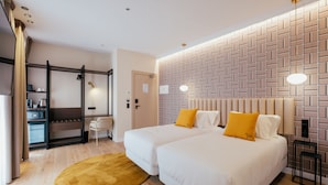 Habitación de hotel con dos camas, piso de madera, pared con diseño de ladrillo y un escritorio con silla.