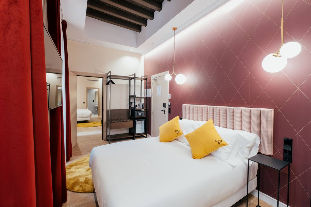 A modern hotel room with a bed, a bedside table, a wardrobe, and a mirror.