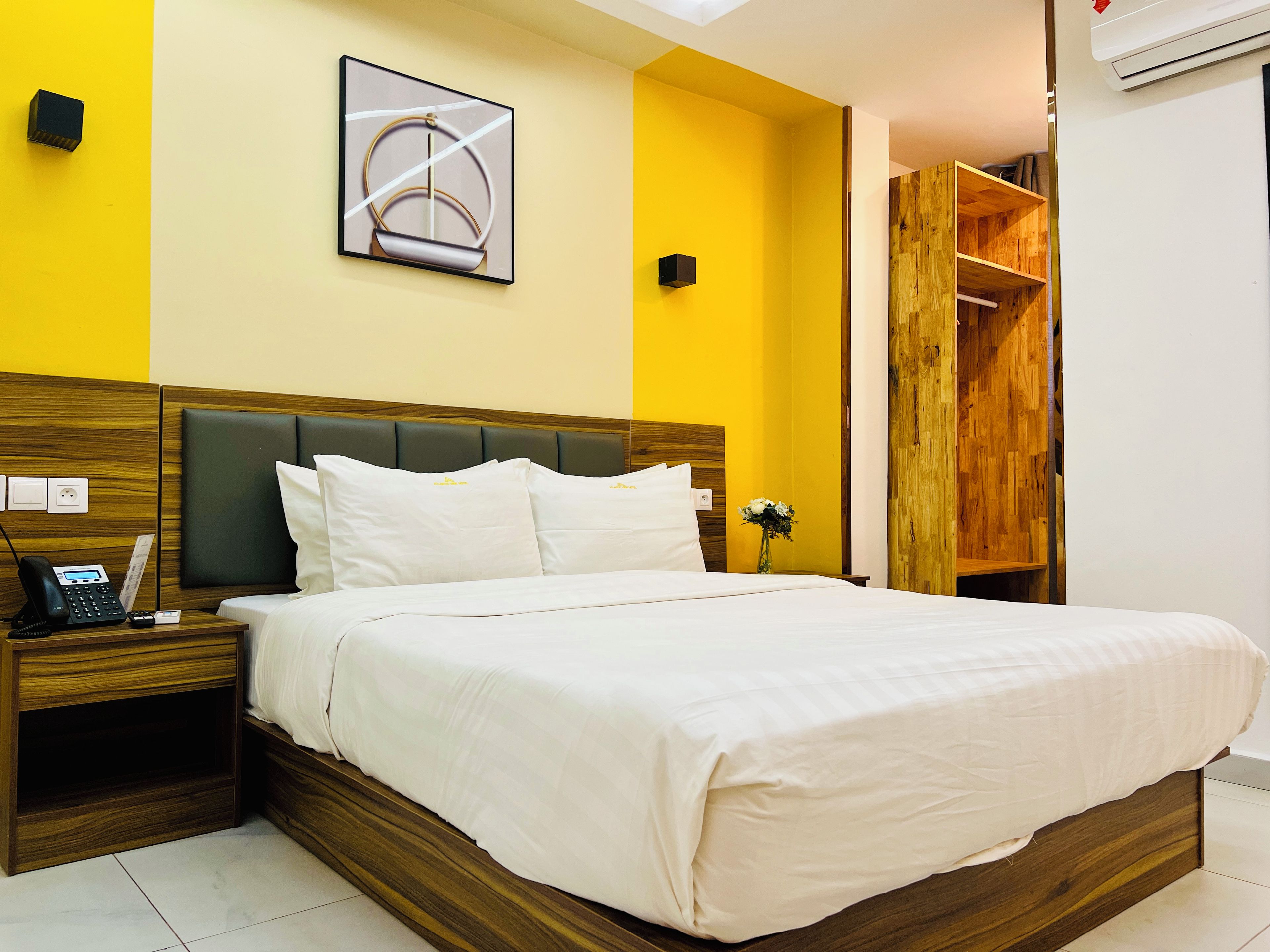 A hotel room with a bed, bedside table, and a wall-mounted artwork.