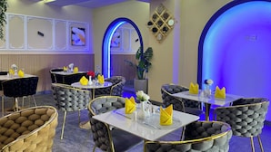 A restaurant interior with round tables, cushioned chairs, and blue lighting. - Atlantic View Hotel (Conakry)