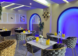 A restaurant interior with round tables, cushioned chairs, and blue lighting. - Atlantic View Hotel (Conakry)