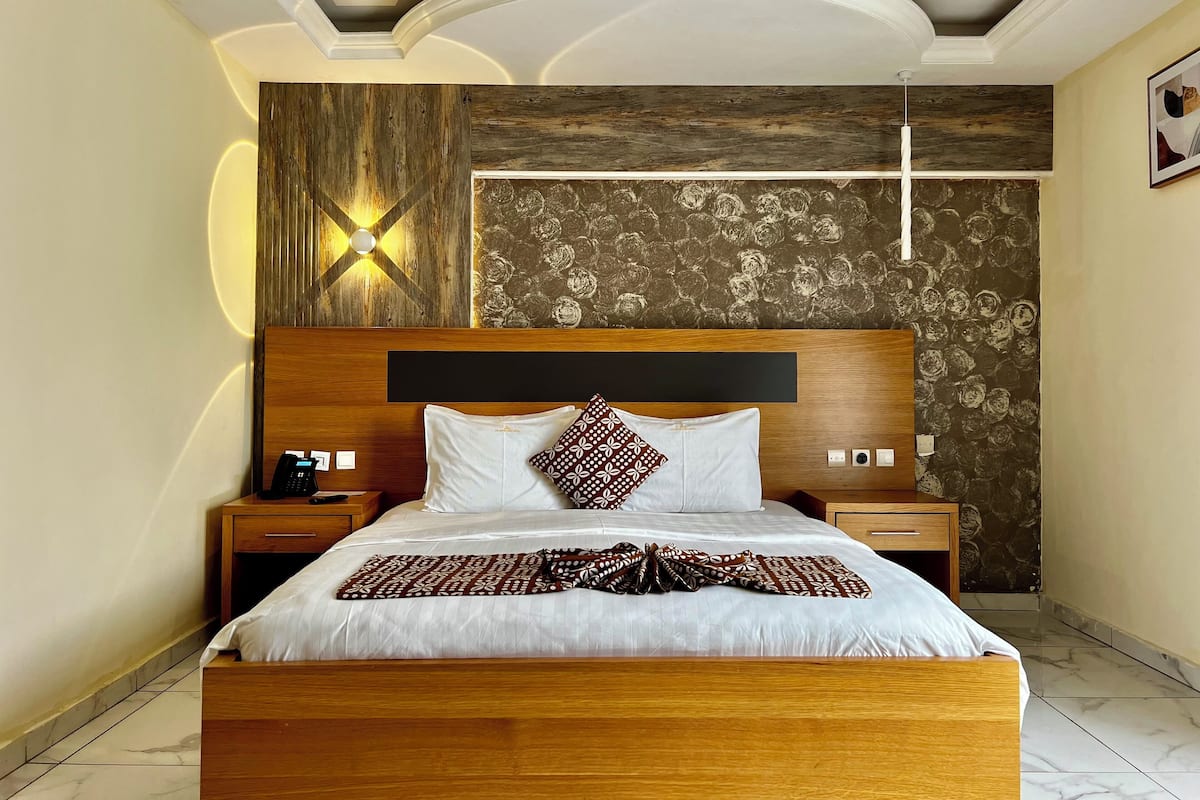 Una cama bien hecha con un edredón estampado, un cabecero de madera y una mesita de noche con un teléfono.