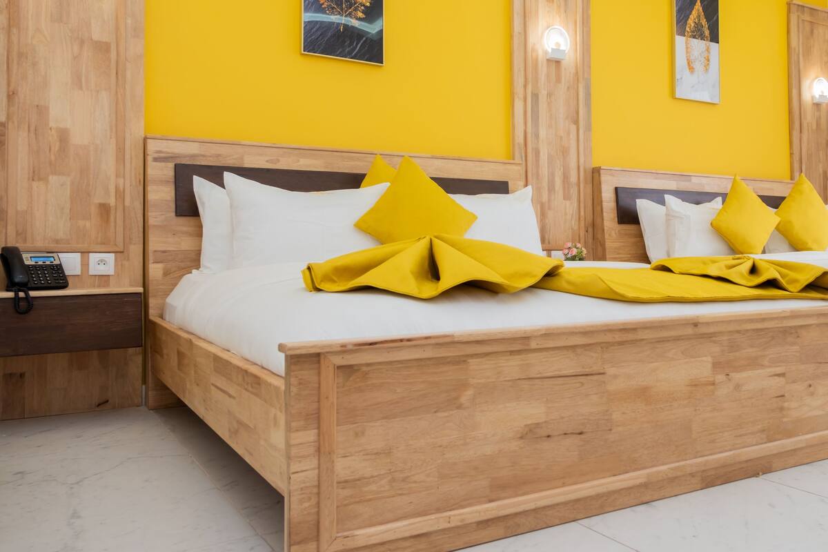 Habitación de hotel con dos camas de madera, paredes de color amarillo brillante y obras de arte en las paredes.