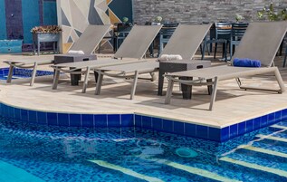 A poolside area with lounge chairs and a small table, surrounded by a tiled pool.