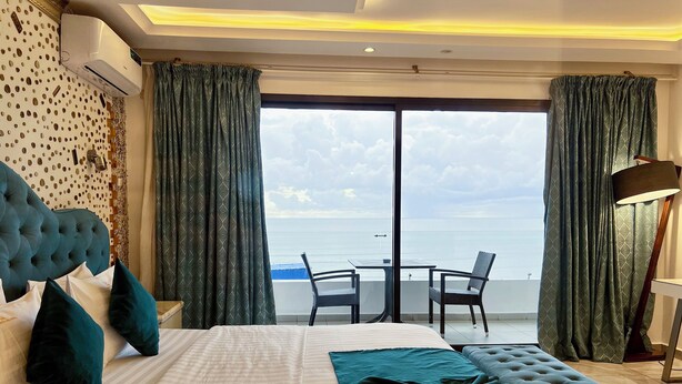 A hotel room with a large bed, a balcony with a table and chairs, and a view of the sea. - Atlantic View Hotel (Conakry)