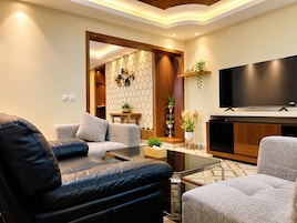 Una sala de estar moderna con un sofá de cuero, un sillón gris, una mesa de centro de vidrio, un televisor de pantalla plana y una pared decorativa con patrones hexagonales.