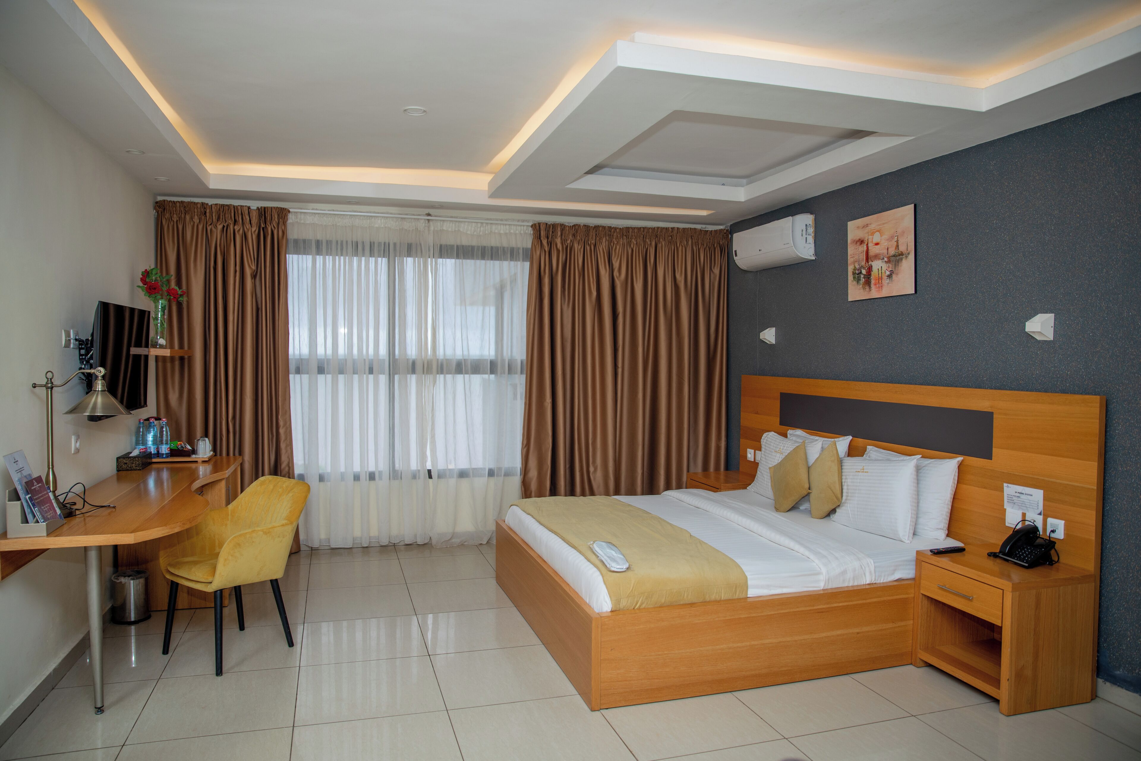 Ein Hotelzimmer mit Bett, Nachttisch, Schreibtisch, Stuhl und einem mit Vorhängen versehenen Fenster.
