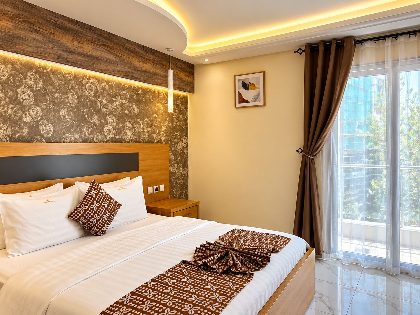 A hotel room with a large bed, a wooden headboard, a nightstand, a wall-mounted light, a framed picture, and a window with curtains.