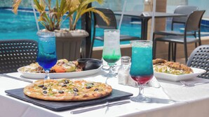 A poolside dining table with a pizza, pasta, and drinks. - Atlantic View Hotel (Conakry)