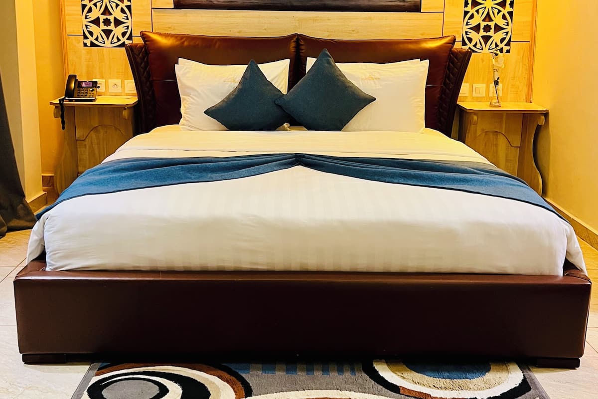 Una cama grande con cabecera de madera, dos mesitas de noche, un cuadro de un barco en la pared y decoración mural estampada.