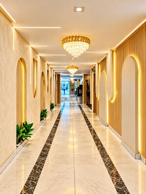Un pasillo de hotel con piso de mármol, iluminación empotrada en la pared y un candelabro central.