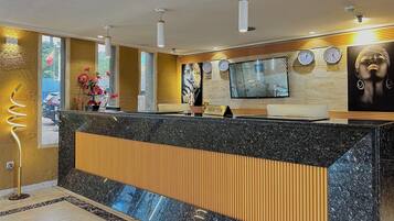 A reception area with a marble counter, wooden paneling, a TV, clocks, and a large window with a view of the outside.